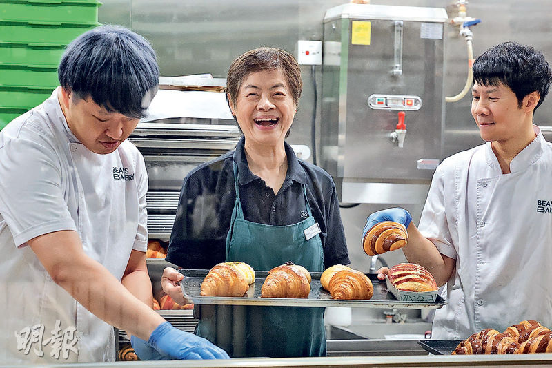 退休後在「荳子烘焙」任職兼職服務員的Auntie Rowena(中)說並非有經濟壓力,但「我想嘗試多做不同事情,證明在這個社會還有用處」。圖為她與工場年輕同事捧出新鮮出爐的麵包。(李紹昌攝)