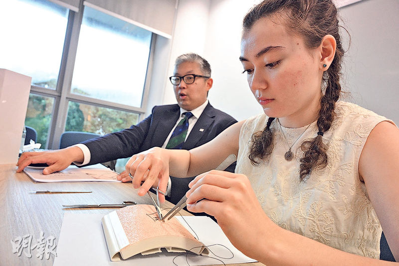 港大醫學院內外全科醫學士課程六年級學生葛倩恩(右)正示範於人造皮膚上做縫合手術。港大醫學院外科學系助理院長(教學法及評核)許長峯(左)說,研究結果發現,曾接受樂器訓練的學生較未曾接受樂器訓練的學生,完成縫針任務的速度快一成,即約25.9秒。(曾憲宗攝)