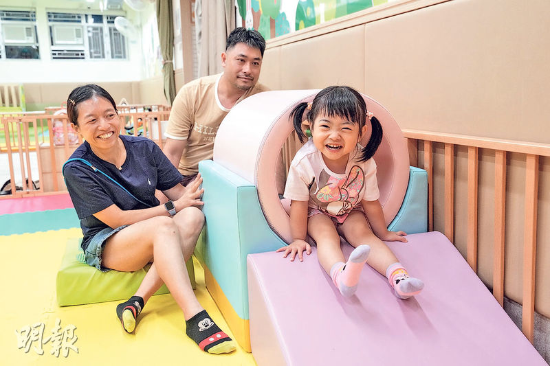 鈳焮(右)在「愛幼坊」日託時間每天均逾10小時,受訪期間她並不怕生,面對記者一直面帶笑容。其父林先生(中)形容這裏是鈳焮「第二個家」,林太(左)亦說託兒是育兒不可或缺的一部分。(廖凱霖攝)